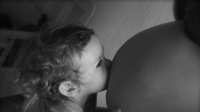 Un bebé besa una barriga de embarazada.