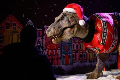 People look at an animated model of a Tyrannosaurus Rex wearing a Santa hat and festive sweater.