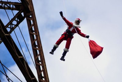 A person dressed as Santa Claus rappels down from a tall bridge.