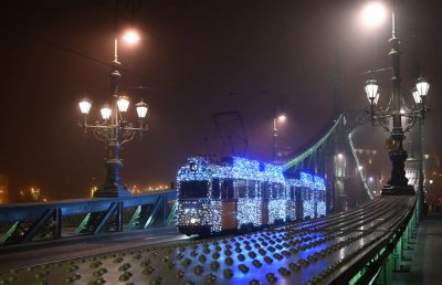 A tram decorated with Christmas lights drives over a bridge.