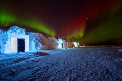A night view of a hotel made from blocks of ice, with the Northern Lights in the sky above.