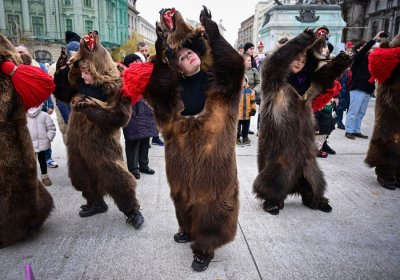 Several people wearing bearskins dance in a city square.