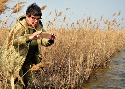 Galyna Minicheva toma una fotografía con un teléfono inteligente entre la hierba de la orilla de un arroyo.
