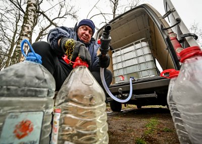 Una persona se agacha detrás de una camioneta para llenar garrafas de agua con una manguera, que llega hasta un tanque de agua en la parte trasera de la camioneta.